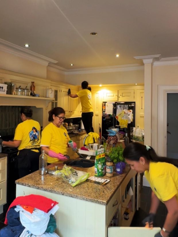 Four cleaners working through a kitchen together, wiping down cupboards and worktops