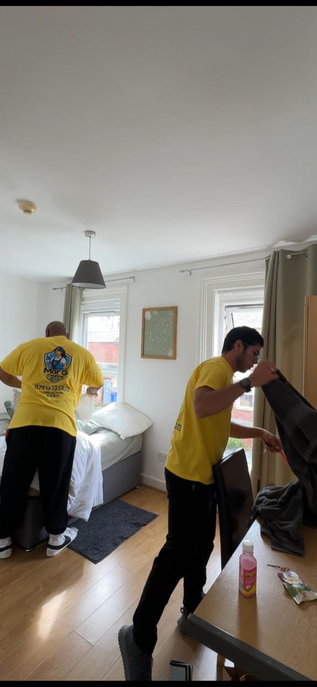 Two cleaners stripping a bed and moving furniture in a bedroom